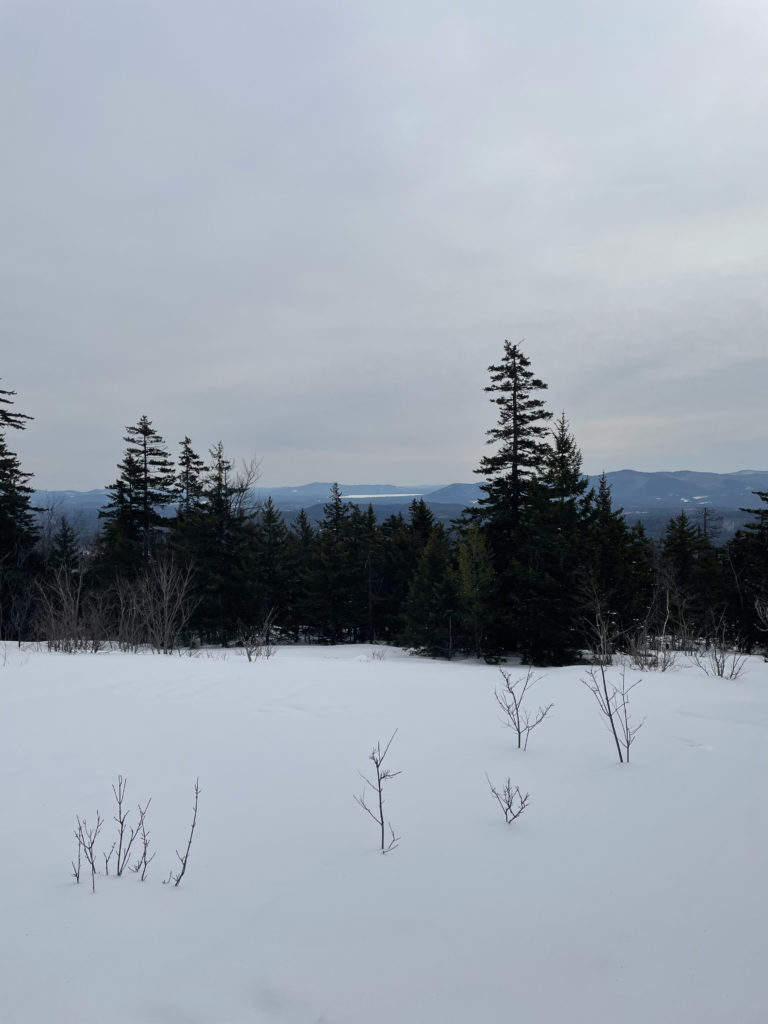 A field of snow and mountains in the distance, seen while hiking Mt. Whiteface in the White Mountains, New Hampshire