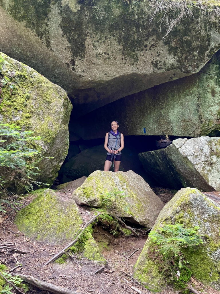 Hiker standing under boulders, seen while hiking Saddleback and The Horn, Western Mountains, Maine