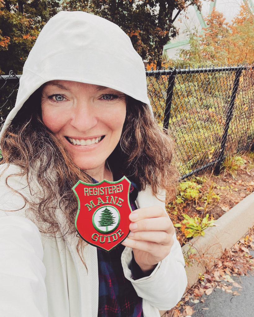 Sarah Holman smiles while holding her red Maine Guide badge.